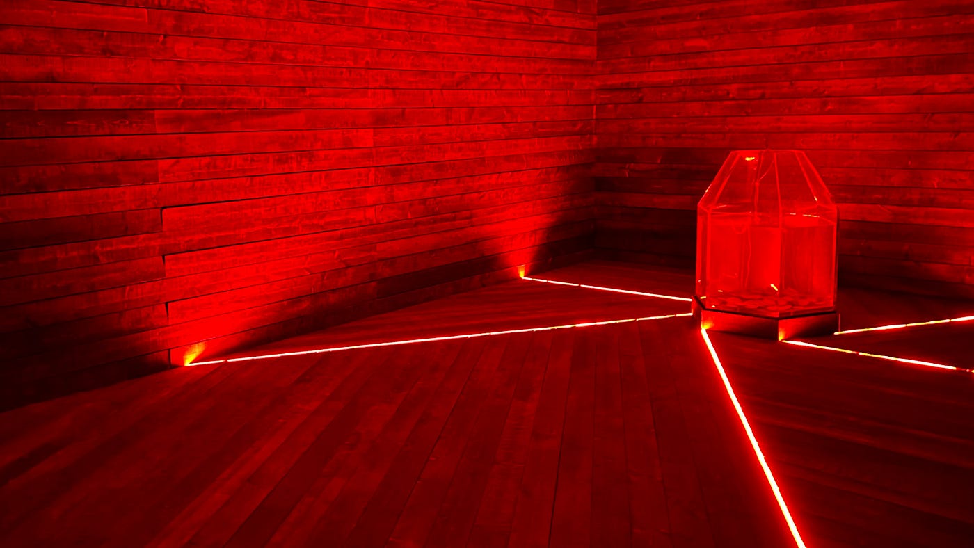 A room is composed of wooden planks: the floor, the walls. Off to one side is a strange glass container. It looks like an aquarium tank, although it’s hexagonal in shape and tapers to a small opening at the top; it’s partially full of liquid and there looks to be some sort of stone along the bottom. Thin openings in between the floor planks shoot out from the edges of the tank. The room is dim, but bright red light emanates from these openings, bathing the room in this red light.