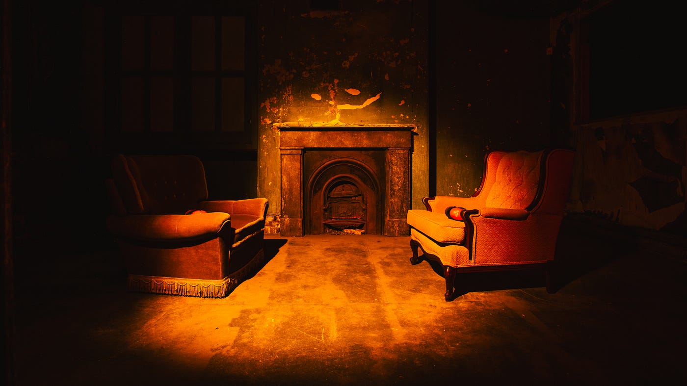 Two armchairs facing each other in front of a fireplace, all in shadow