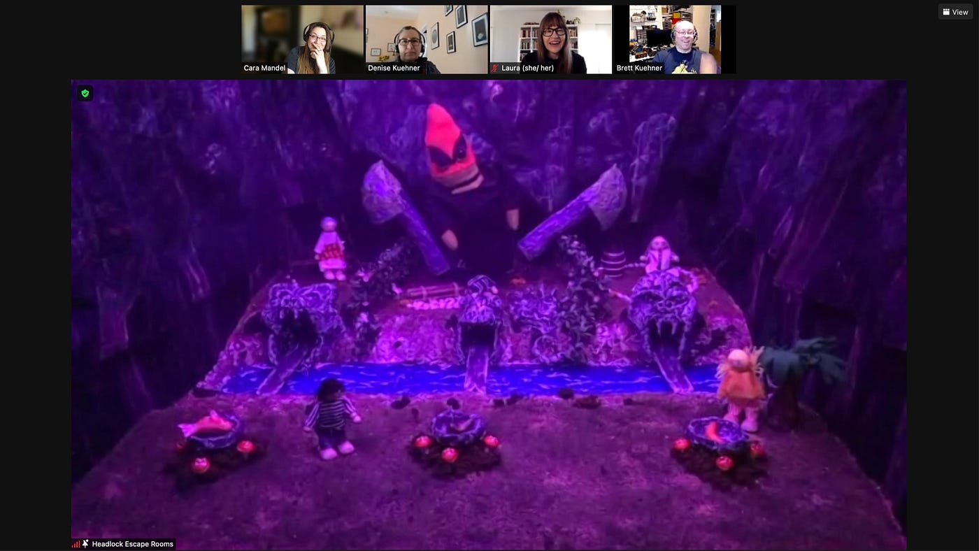 This screengrab shows a row of thumbnail images at the top: a group of four players, each in separate locations, are laughing. Underneath them is the view inside a diorama. The setting is a riverbank, with three bridges. Villagers are on both sides of the river and each bridge is the tongue of a different animal statue on the other side of the river. The mood is ominous: the scene is bathed in deep violet light, which emphasizes the neon orange of an angry looking mushroom king.